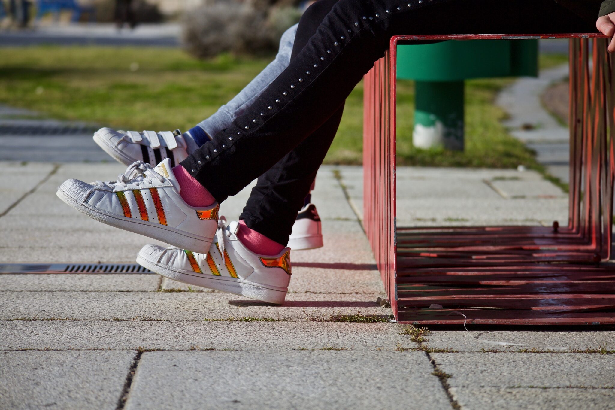 Pies de dos adolescentes con una adidas sentadas en un banco de un parque