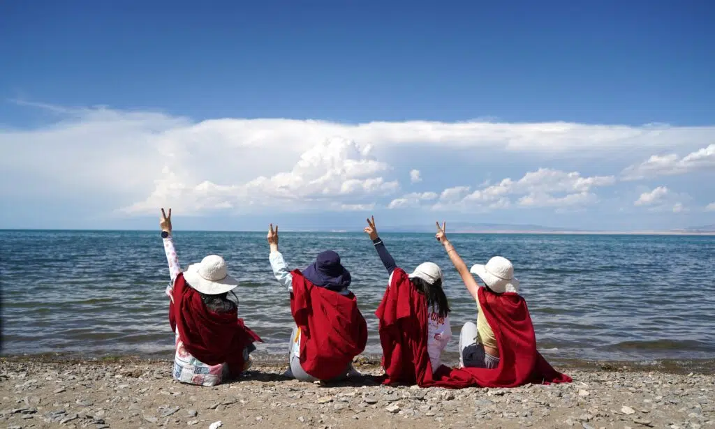 cuatro personas de espalda a la orilla del mar con un brazo levantado y con pañuelos rojos