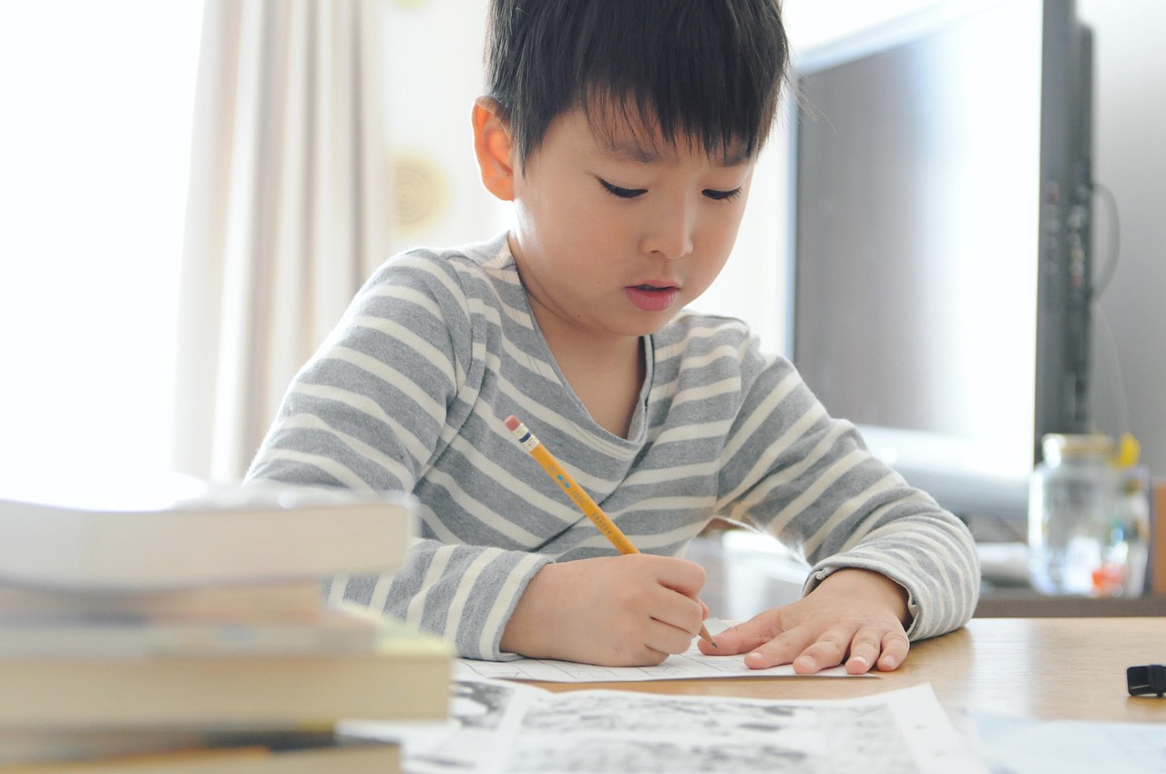 niño oriental haciendo deberes con una camiseta de rayas gris y blanca