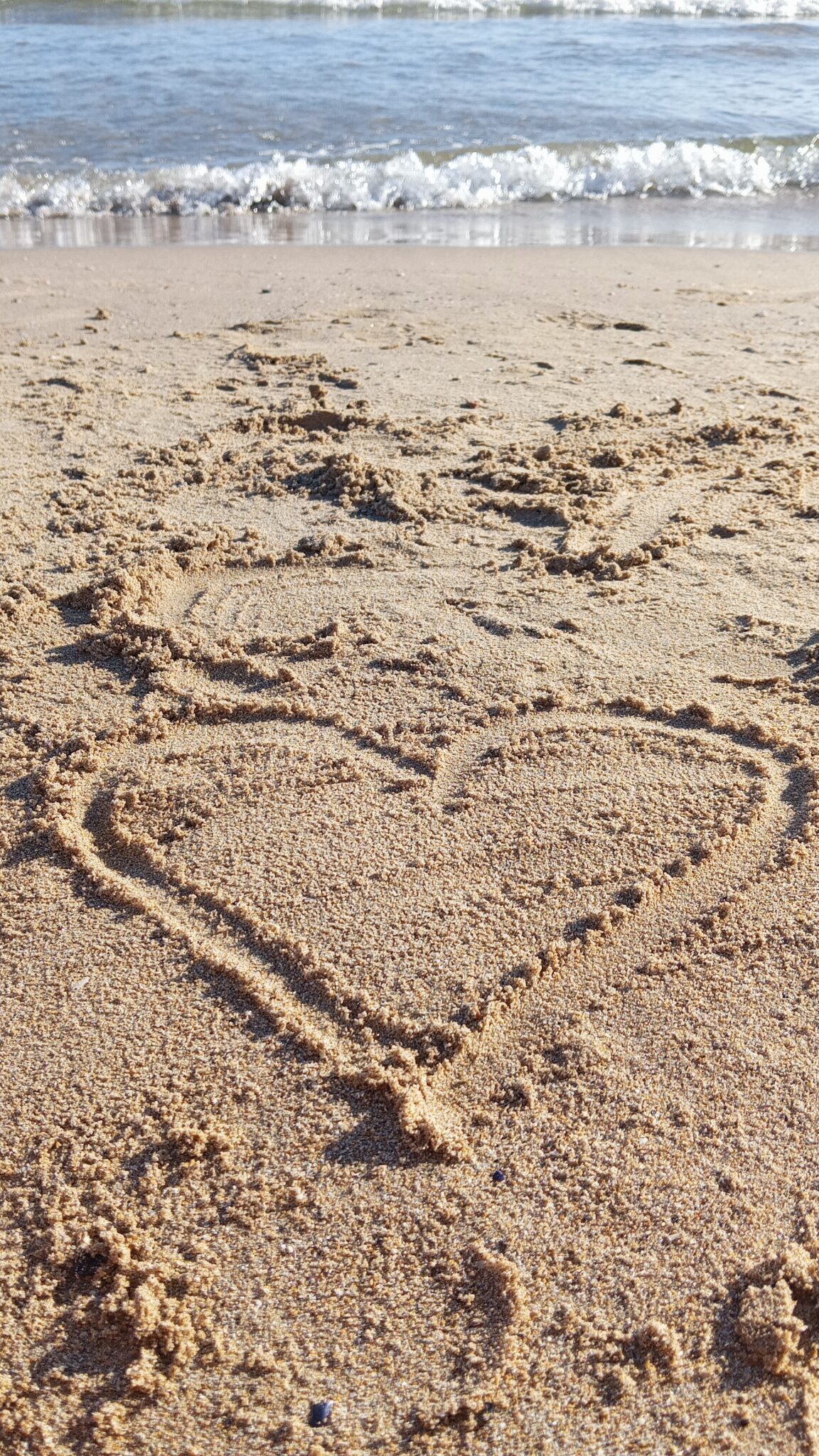 Corazón dibujado en la orilla del mar con una ola al fondo