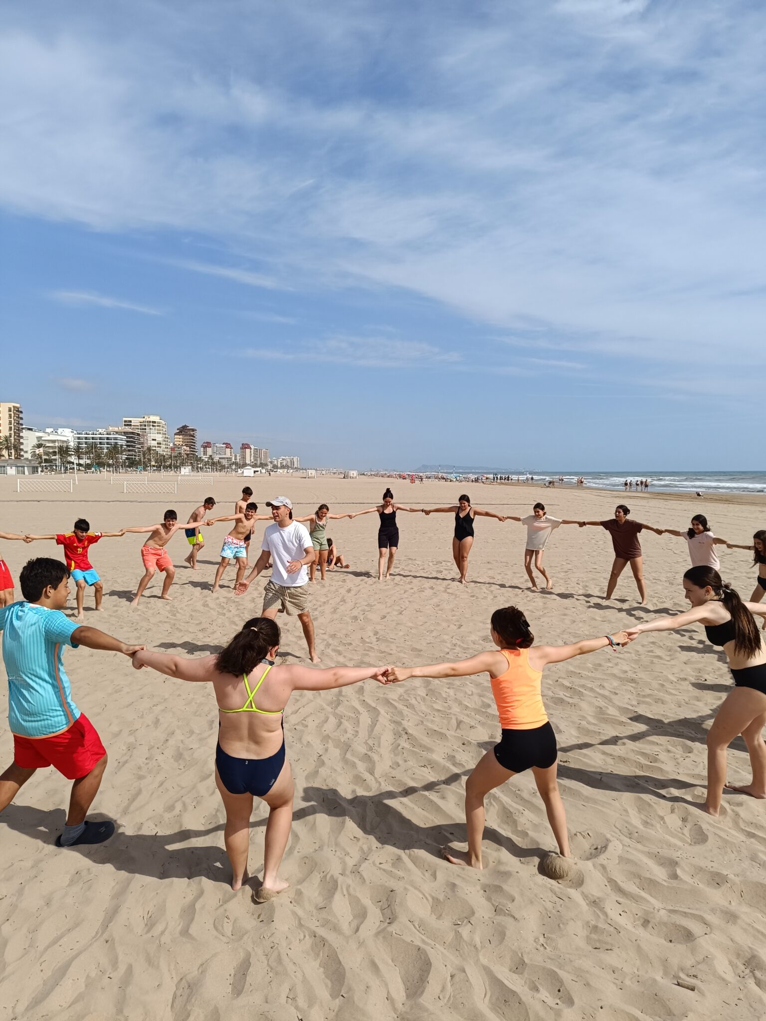 Grupo de chavales en la playa jugando en un circulo todos cogidos de la mano