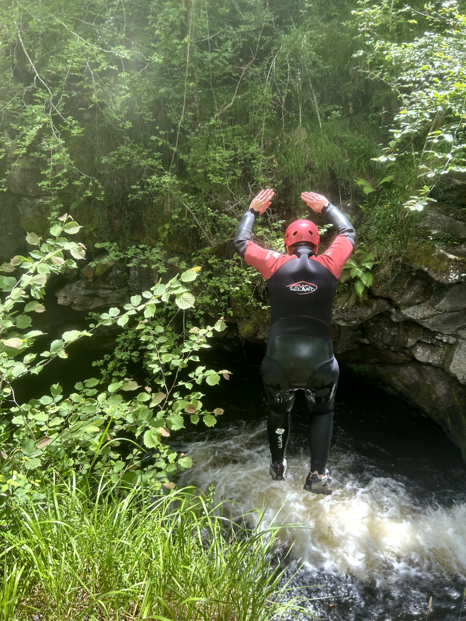 persona con neopreno de espaldas saltando en un barranco con agua
