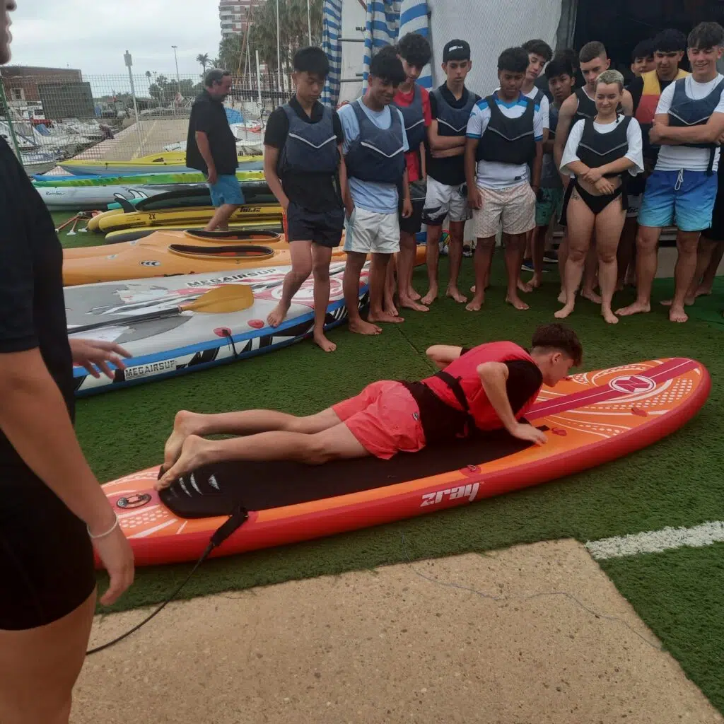Un alumno realizando una practica en tierra de como ponerse en la tabla de paddle surf