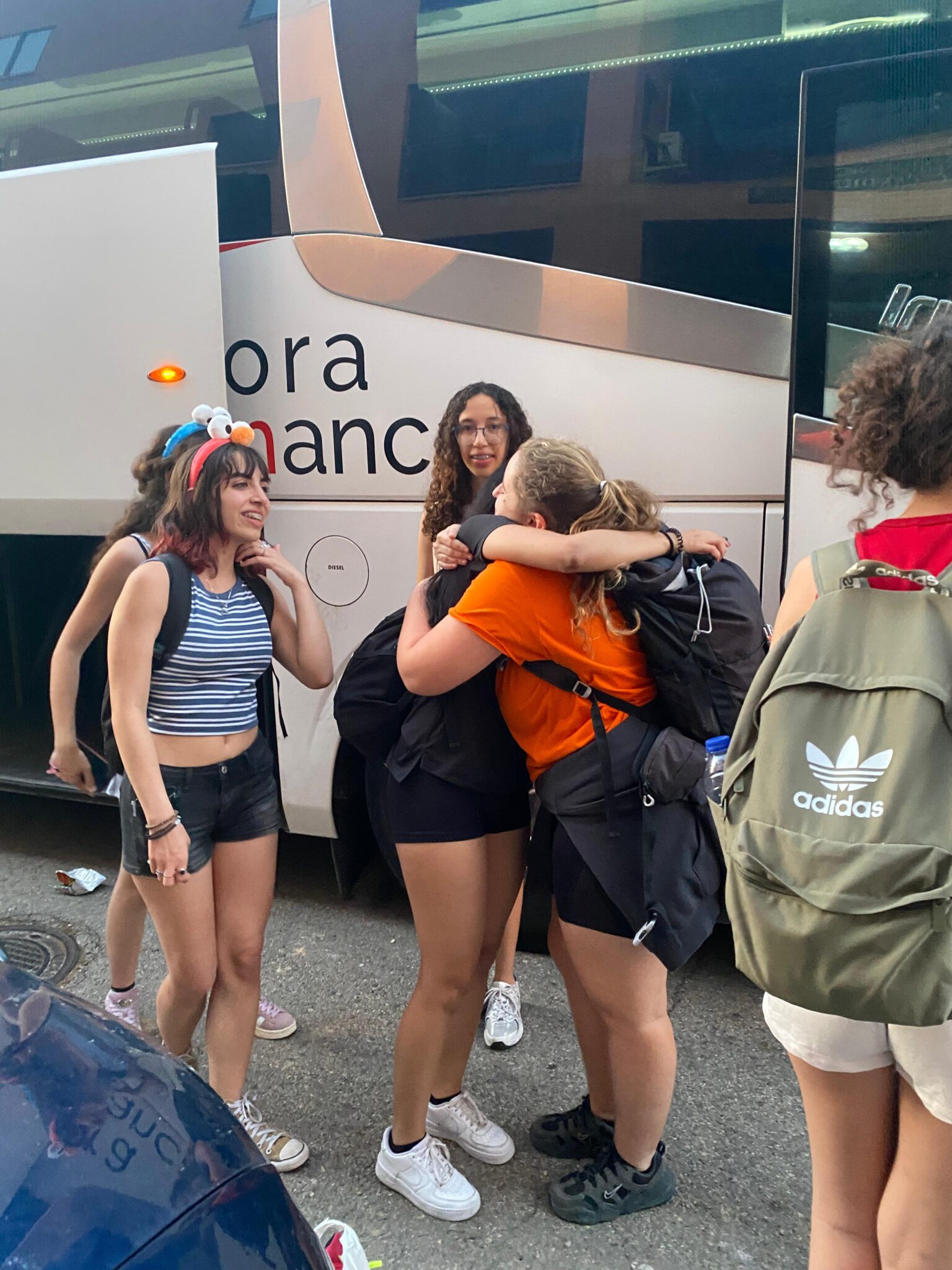 Tres adolescentes que se despiden con un abrazo de su coordinador de viaje