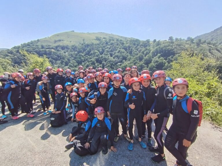 grupo de primaria vestidos para hacer descenso de barrancos con fondo de bosque y cielo azul