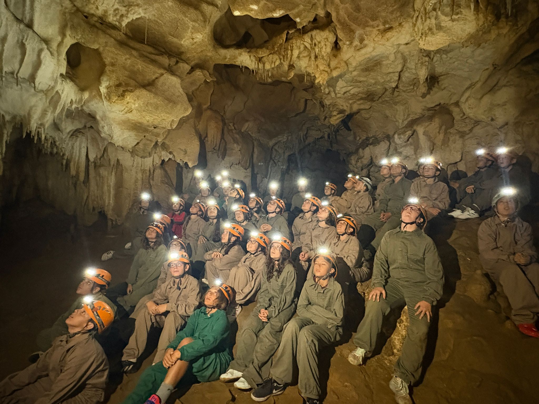 grupo de primaria dentro de una cueva vestidos con monos y sus frontales encendidos