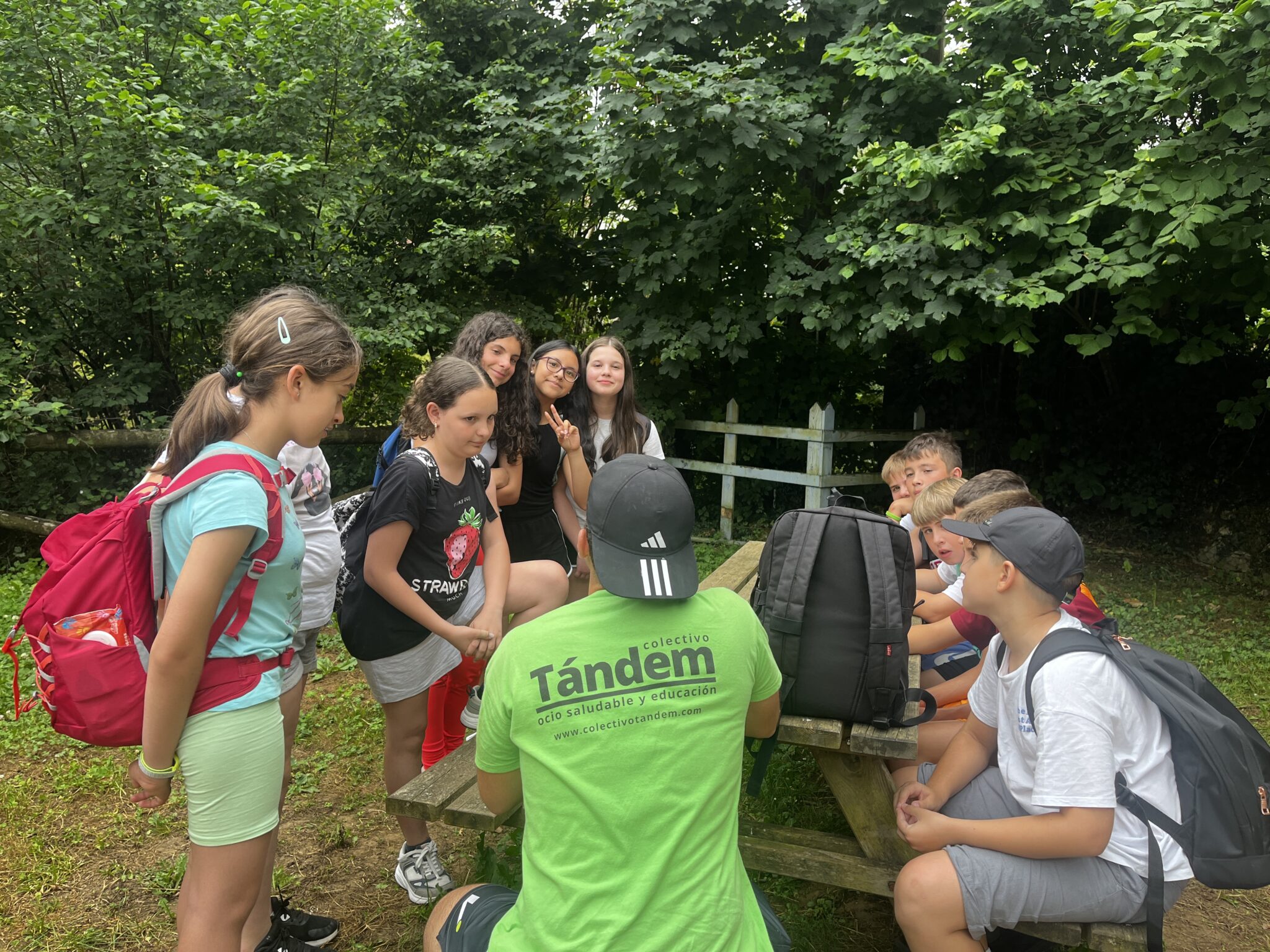 monitor de Colectivo de espalda con la camiseta corporativa y su grupo de chavales hablando