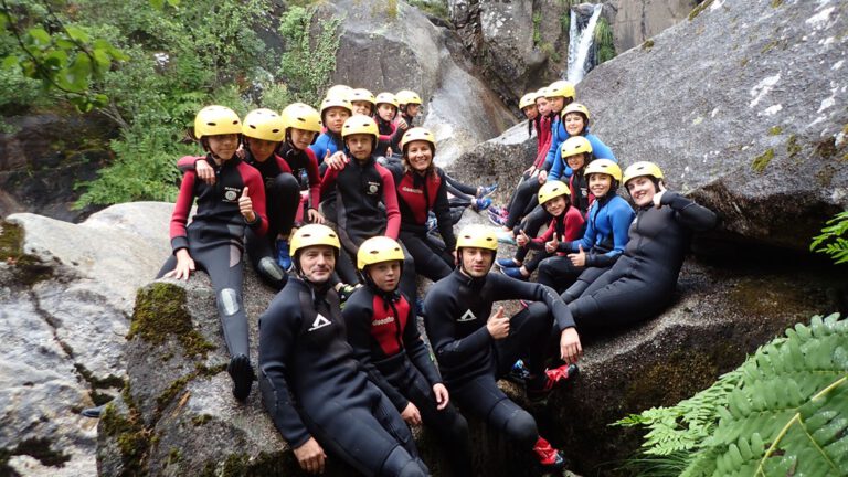 grupo de 6º de primaria y profesores con neoprenos y cascos sentados en unas rocas