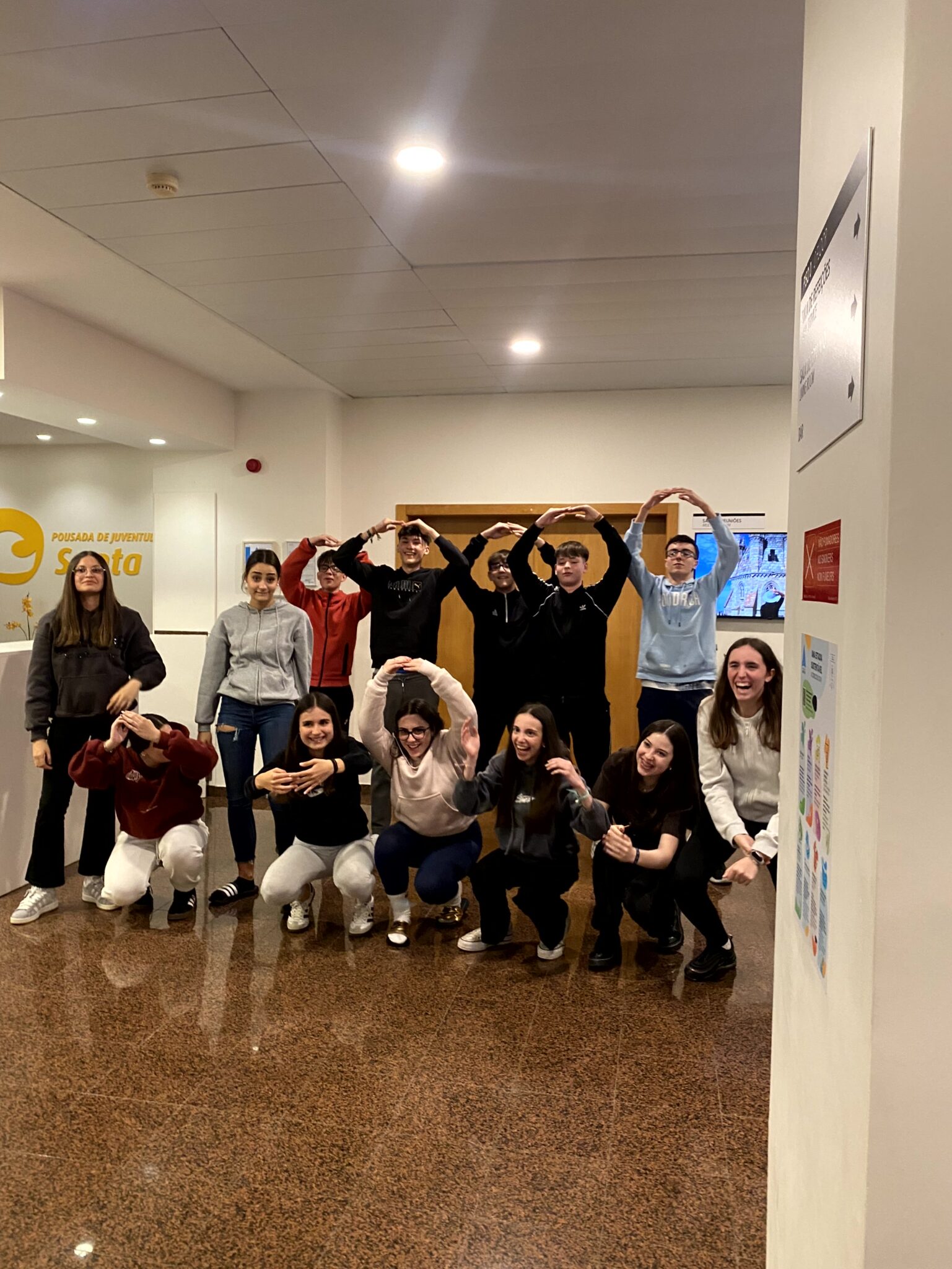 Grupo de chavales de secundaria en el hall de un albergue haciendo una figura con su cuerpo