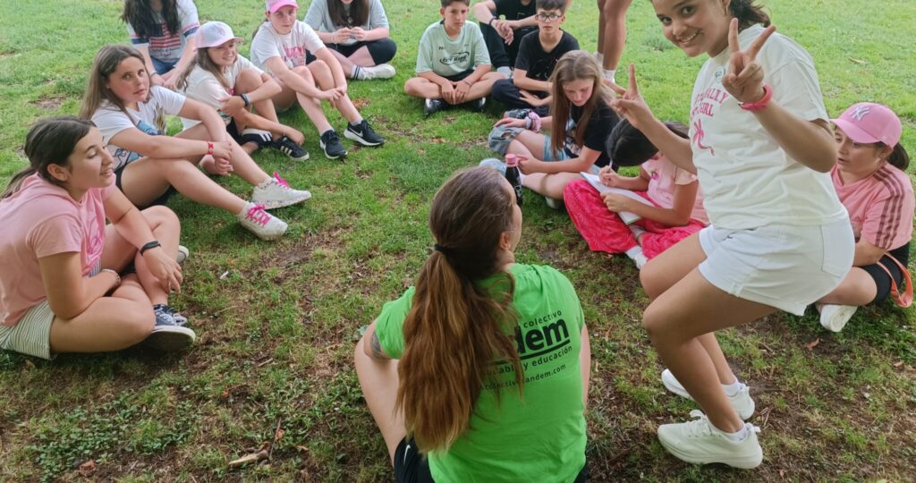 grupo de niños de primaria sentados en un parque en círculo con su monitora de espalda