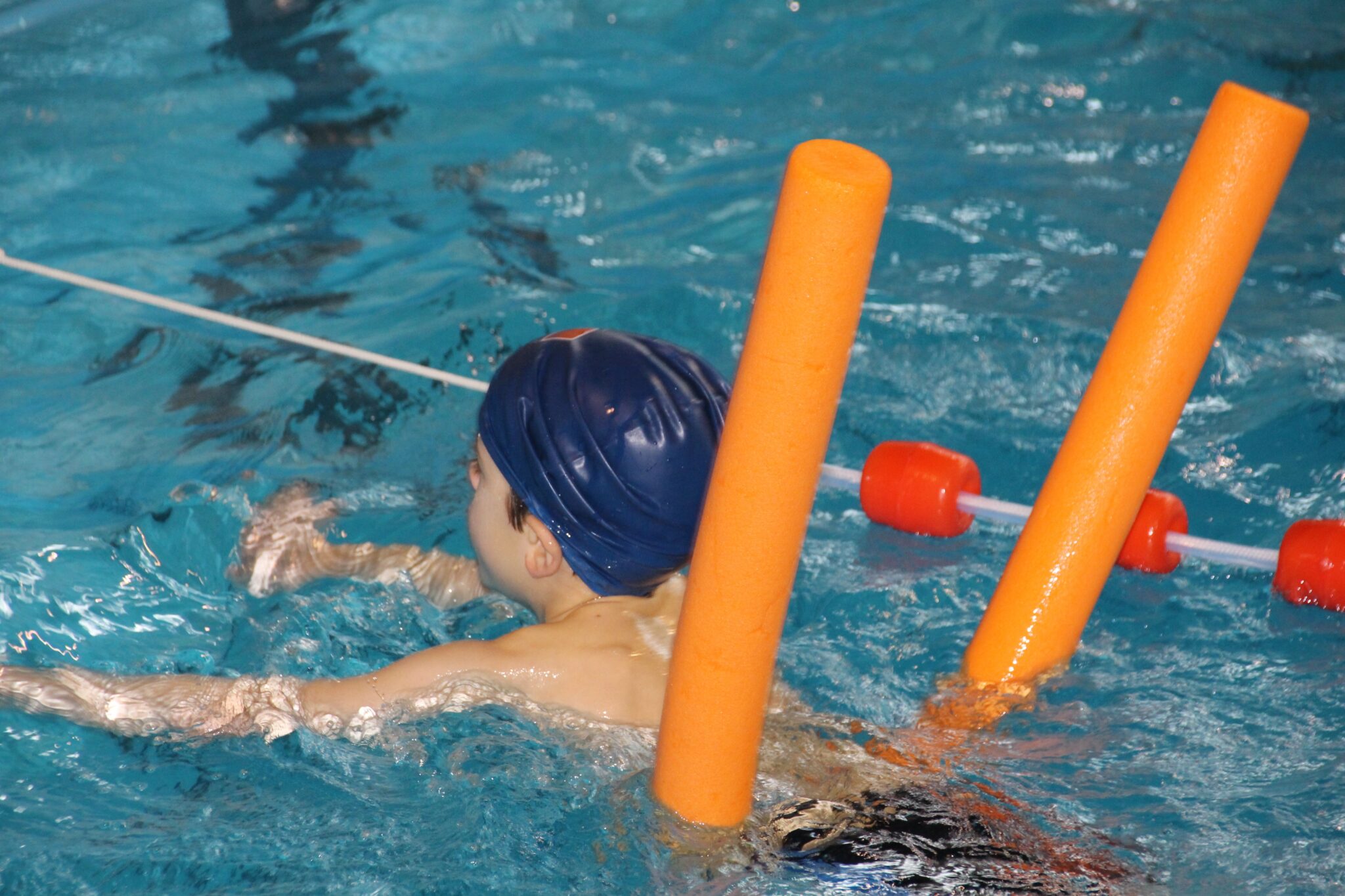 clase de natacion de un niño con gorro azul