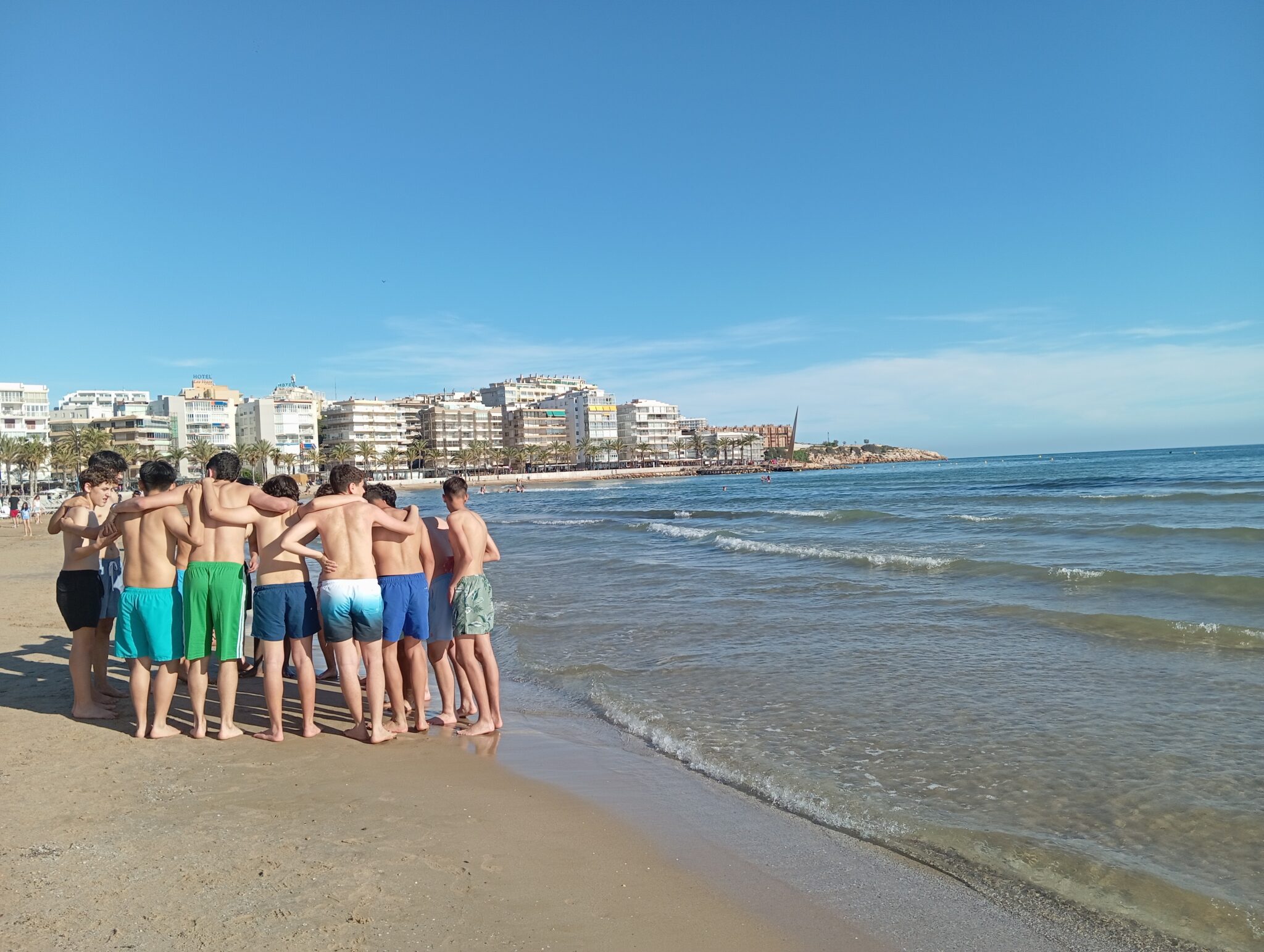grupo de chicos de espaldas abrazados en la orilla de la playa