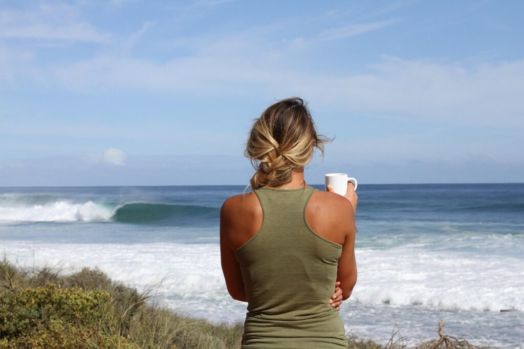 Mujer que sostiene una taza y que esta de espaldas con el fondo del mar