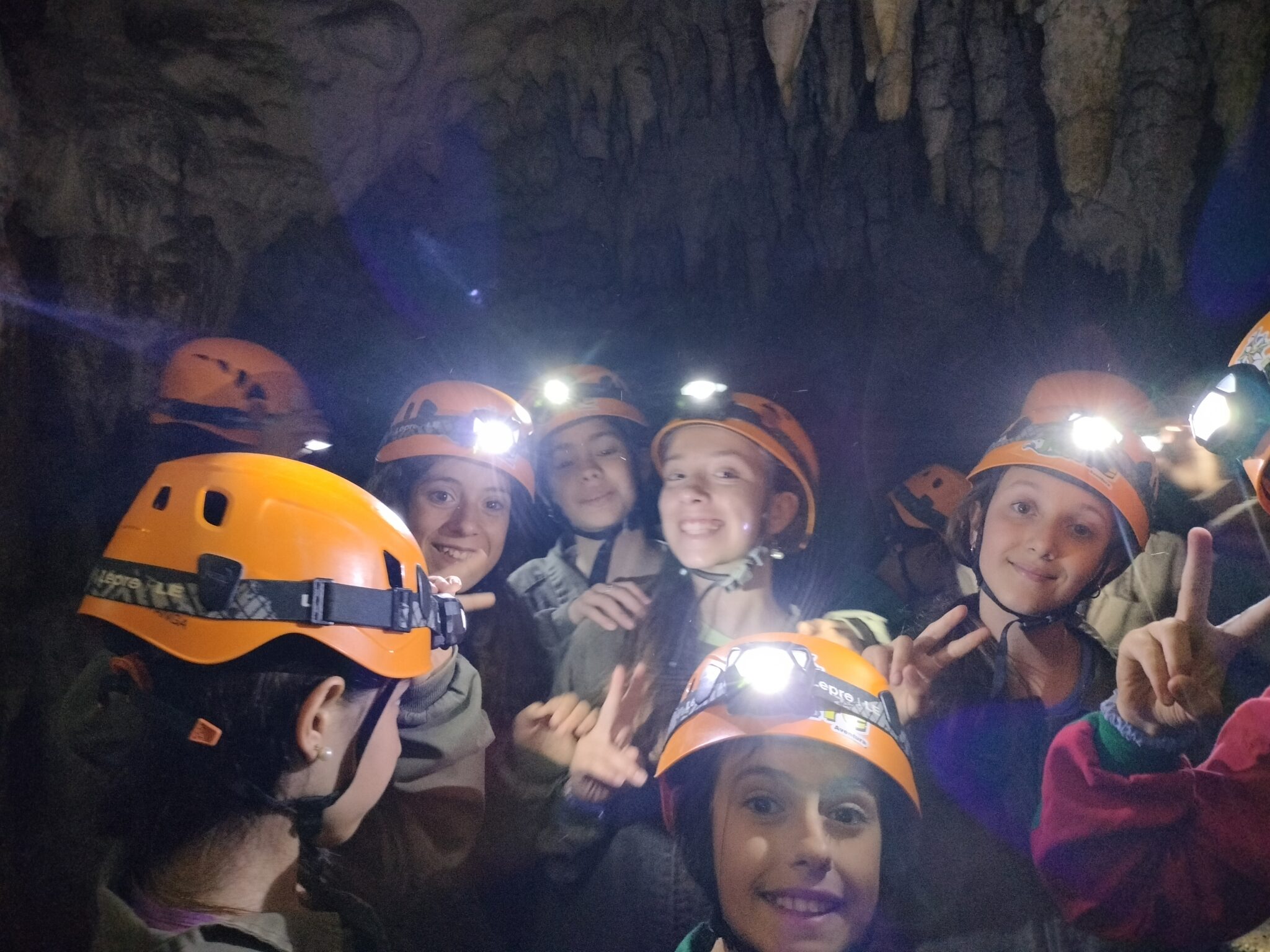 Grupo de primaria en un viaje de fin de curso dentro de una cueva de espeleología con cascos naranjas
