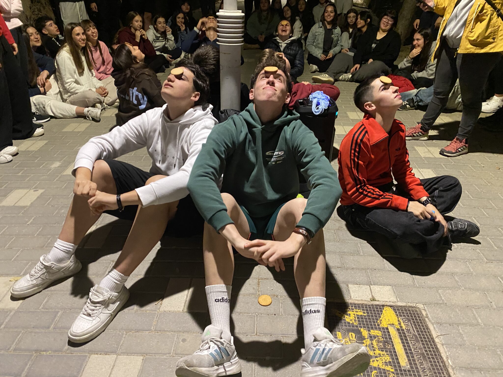 tres adolescentes sentados en el suelo jugando con una galleta en la frente