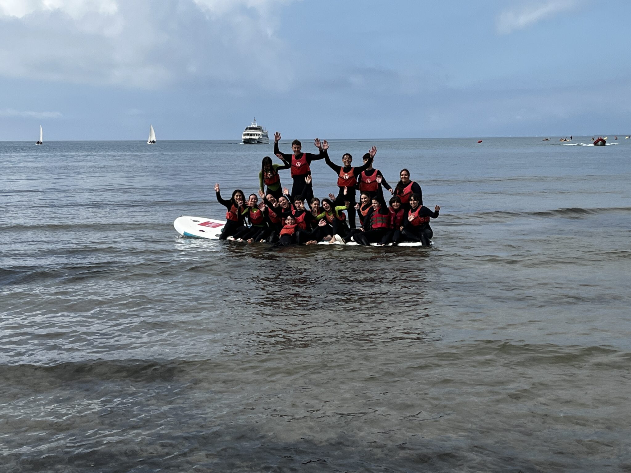 grupo de secundaria encima de una tabla de paddlesurf con sus neoprenos negros y chalecos rojos