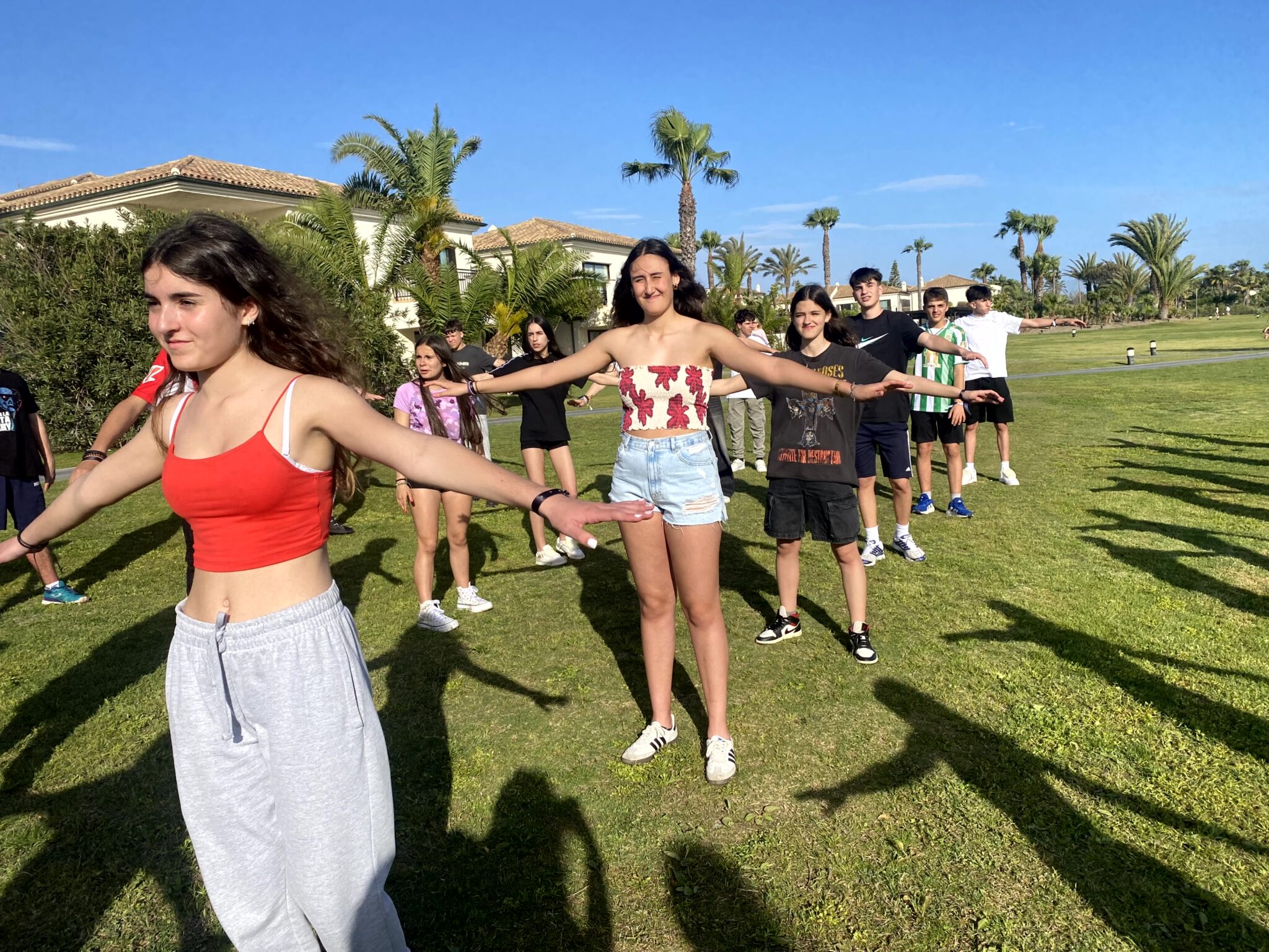 grupo de secundaria en un jardín haciendo ejercicios con los brazos en cruz