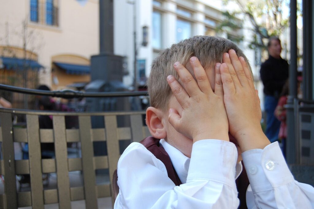 un niños sentado tapándose la cara con las manos