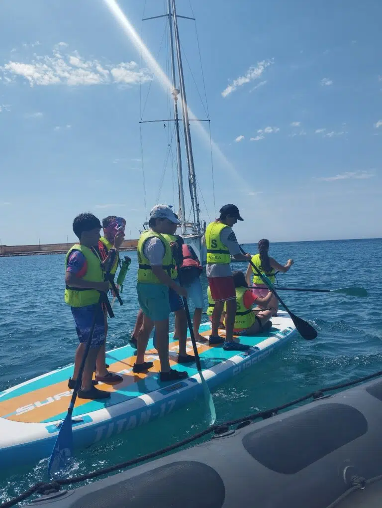 grupo de primaria sobre una tabla de paddle surf con chalecos amarillos y de espaldas