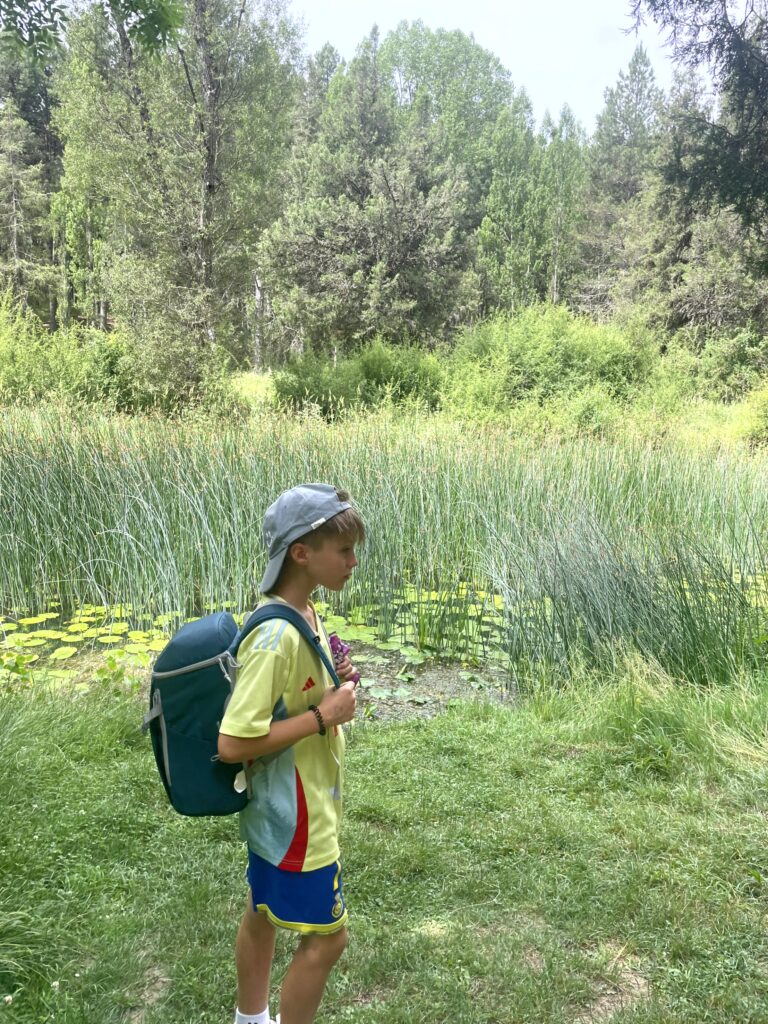 chaval de perfil con su mochila y gorra delante de un lago