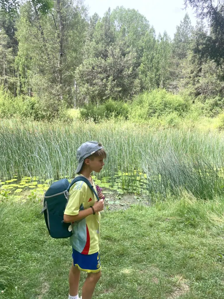 chaval de perfil con su mochila y gorra delante de un lago