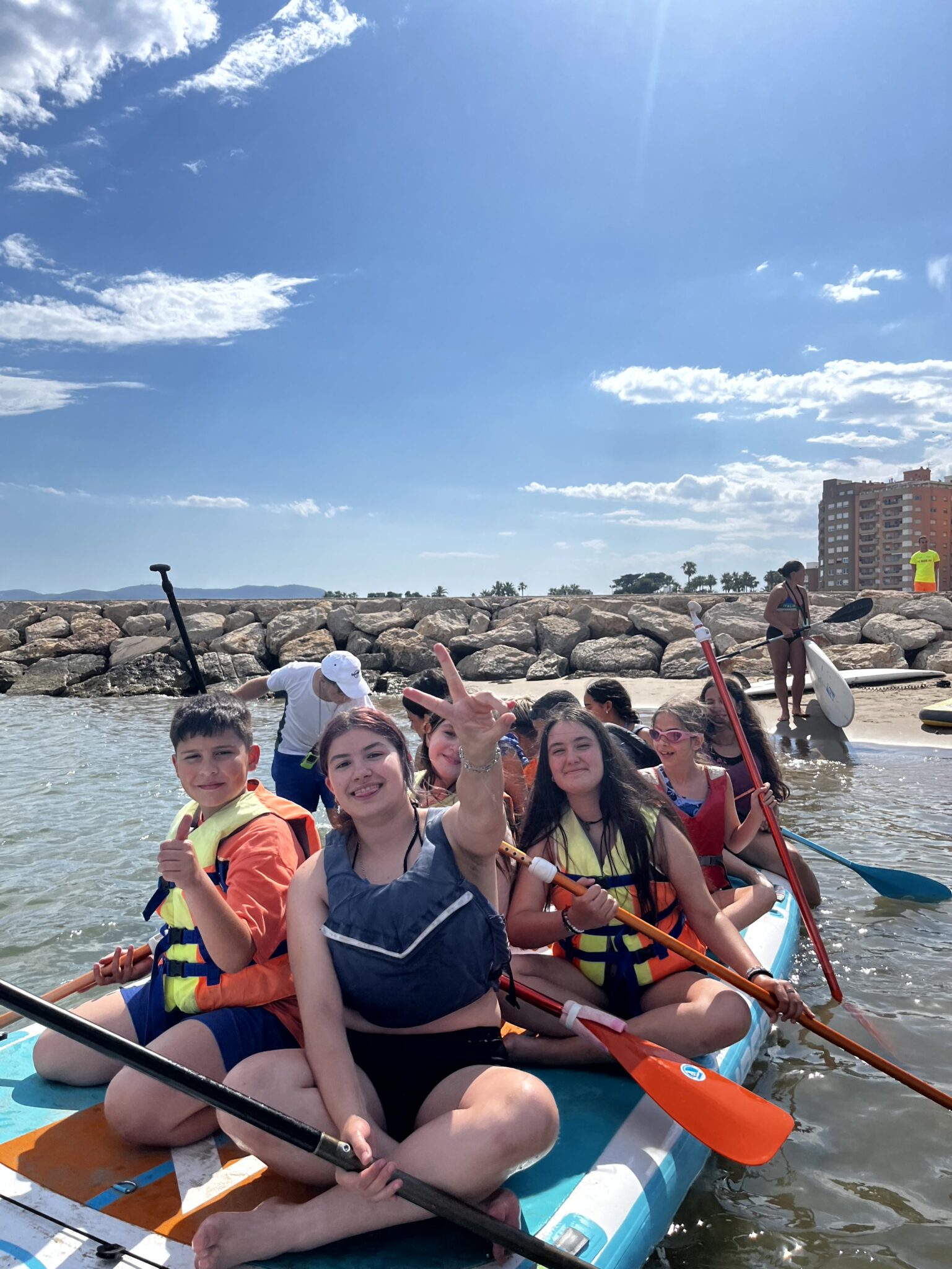 grupo de secundaria sentados en una tabla de paddle surf saliendo de la playa