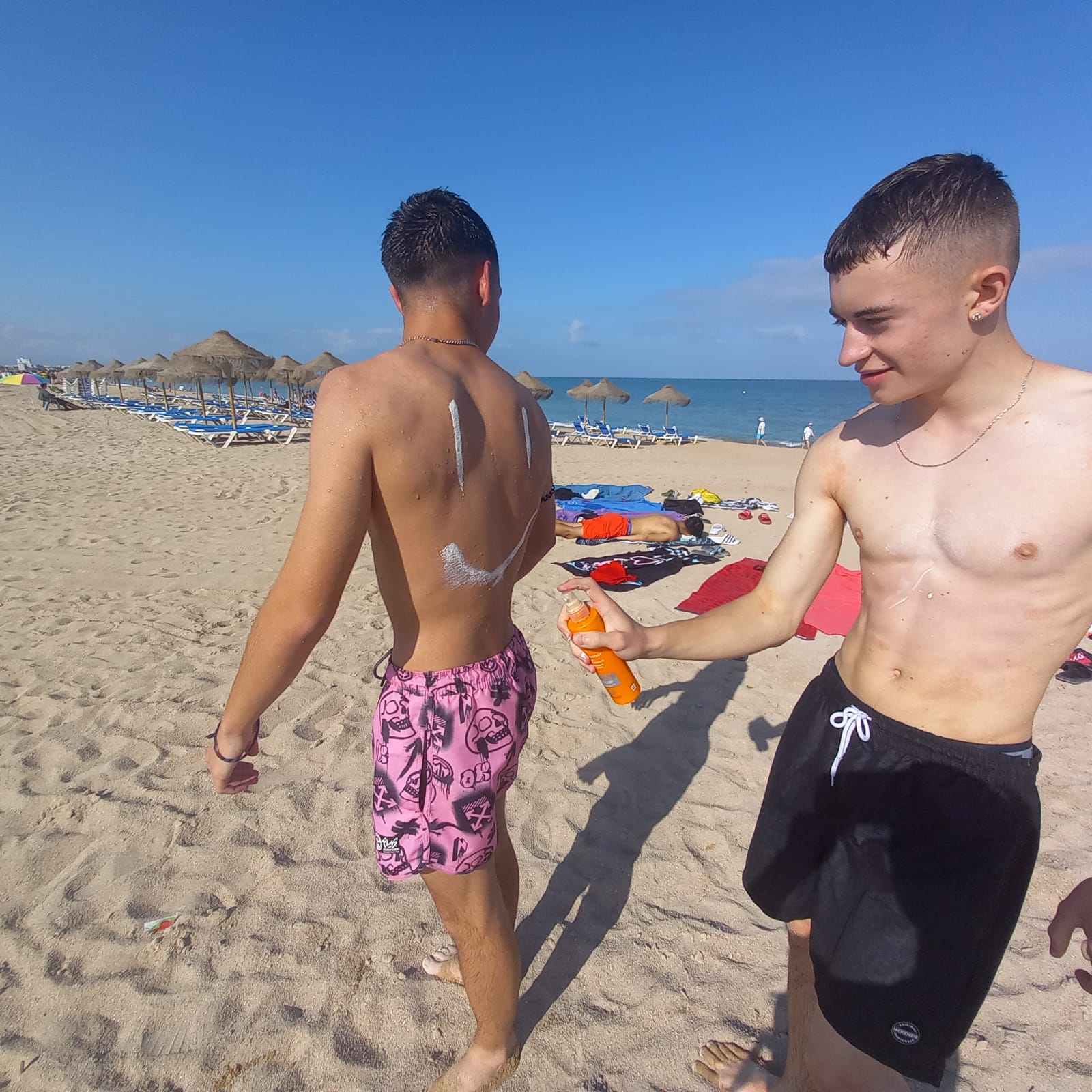 un adolescente en la playa haciendo una cara con la crema solar en la espalda de otro