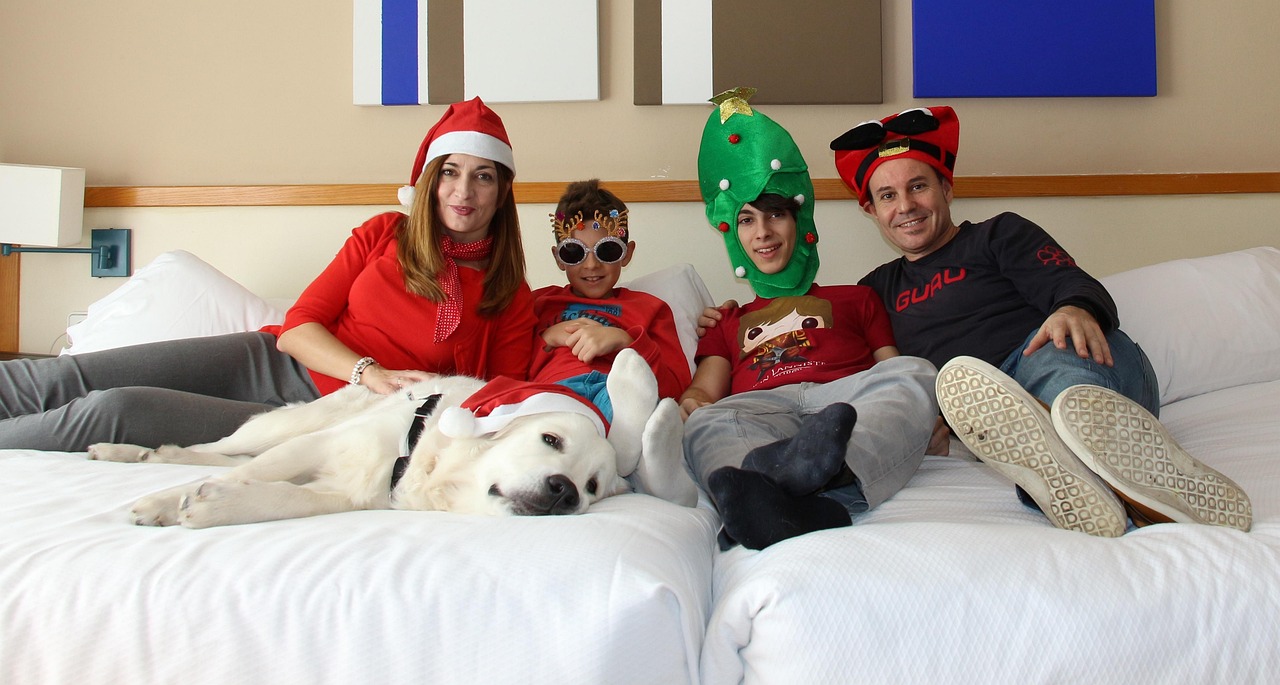 una familia de dos adolescentes subidos en la cama con gorros navideños y un perro