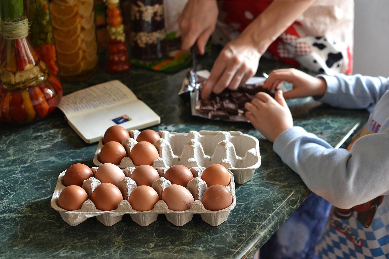 una mesa de cocina con unos huevos y una manos infantiles y otras adultas partiendo chocolate