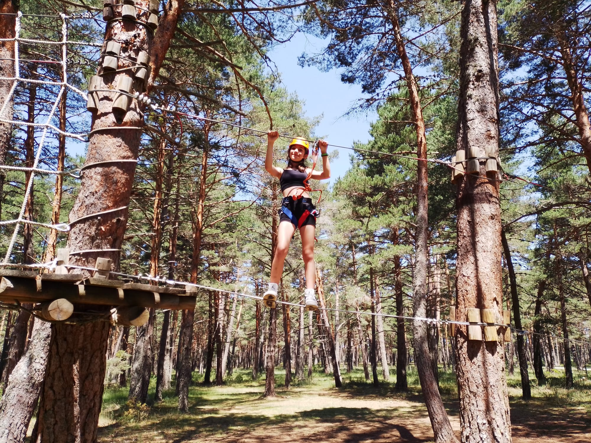 niña de primaria subida a un puente tibetano entre dos pinos