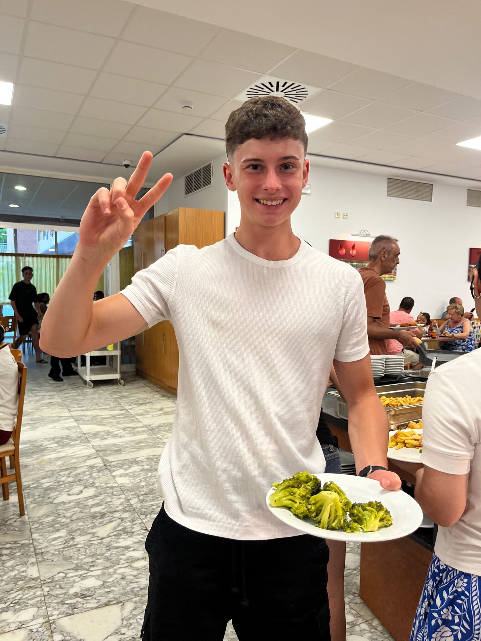 adolescente sonriente en un comedor de hotel con una plato de brecol al vapor