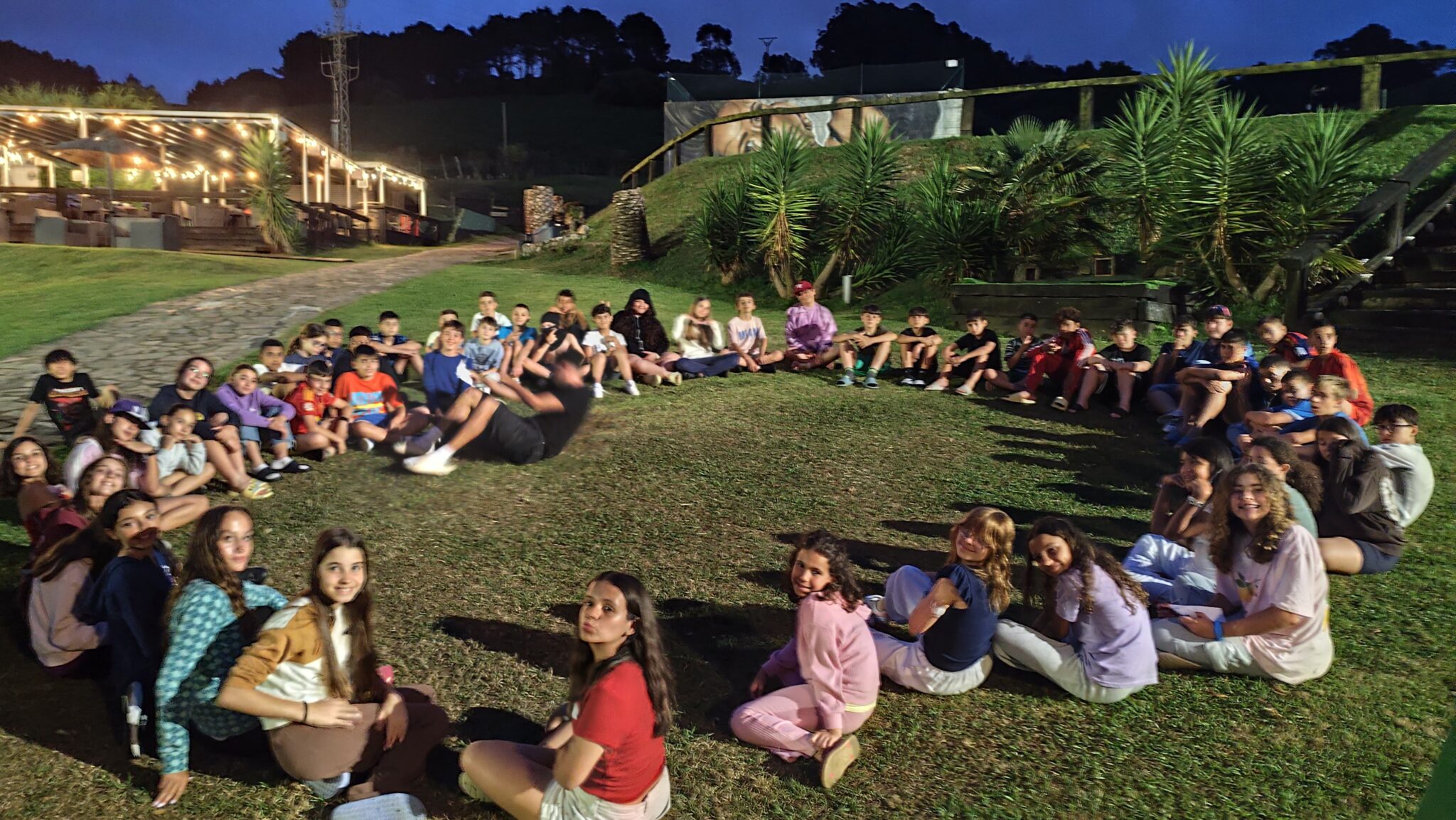 grupo de primaria sentado en circulo en el jardin de un hotel de noche