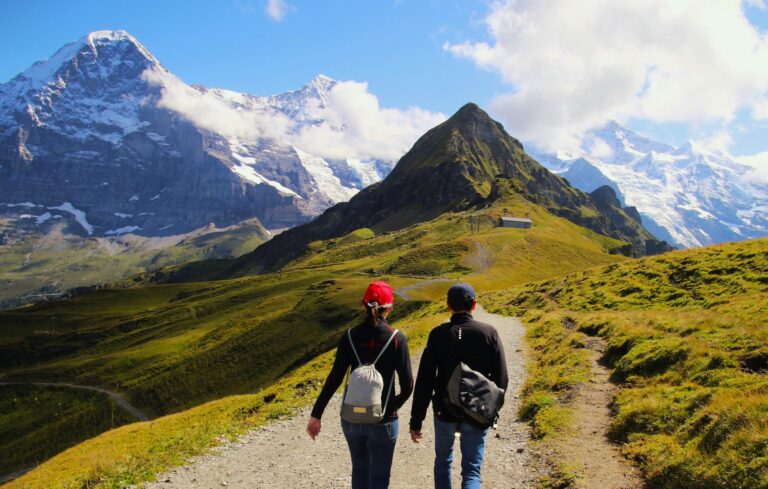 dos personas de espaldas con gorras, haciendo senderismo por una montaña