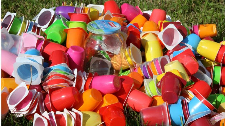 muchos envases de yogures de colores variados con un tarro de cristal vacío en el medio en el campo