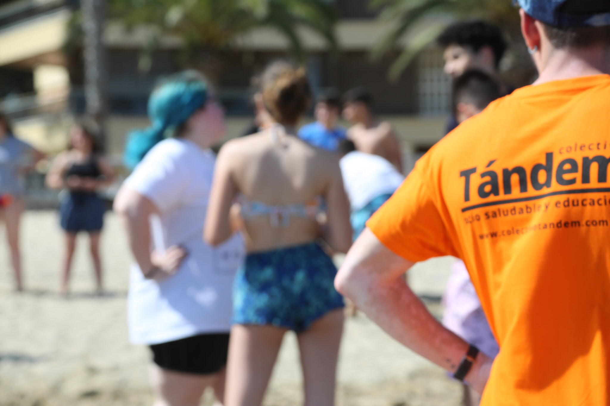 Grupo de adolescentes en la playa desenfocados y en primer plano camiseta naranja de espalda de colectivo tandem