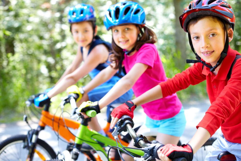 primer plano de tres niños en sus bicicletas con guantes y cascos de colores vistosos