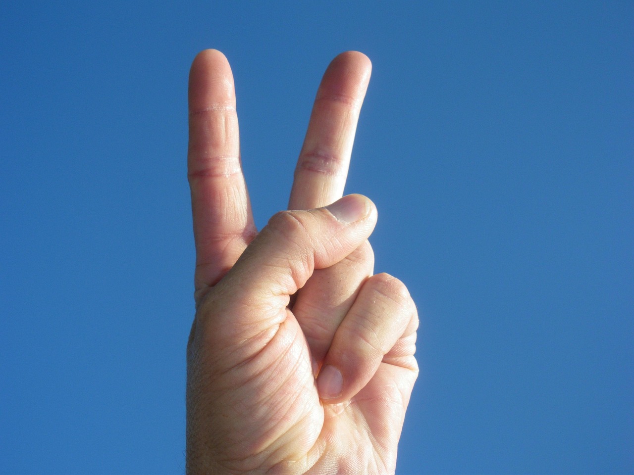 primer plano de una mano con el símbolo de paz o v de victoria, fondo azul