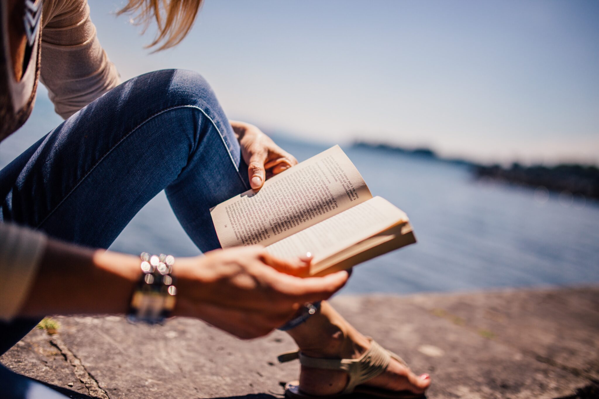 mujer que lee un libro sobre un dique encima del mar