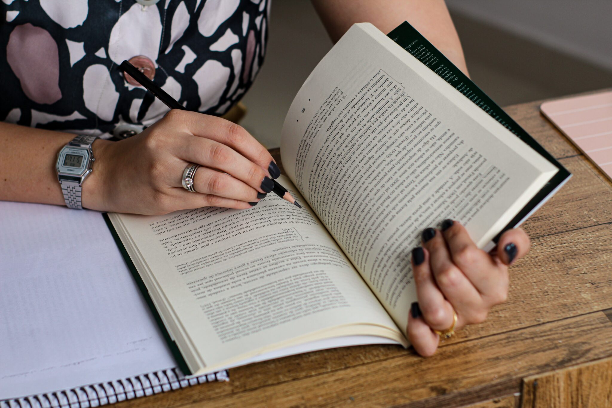 un libro sostenido por una mujer con uñas pintadas en negro que lleva un lápiz en la mano