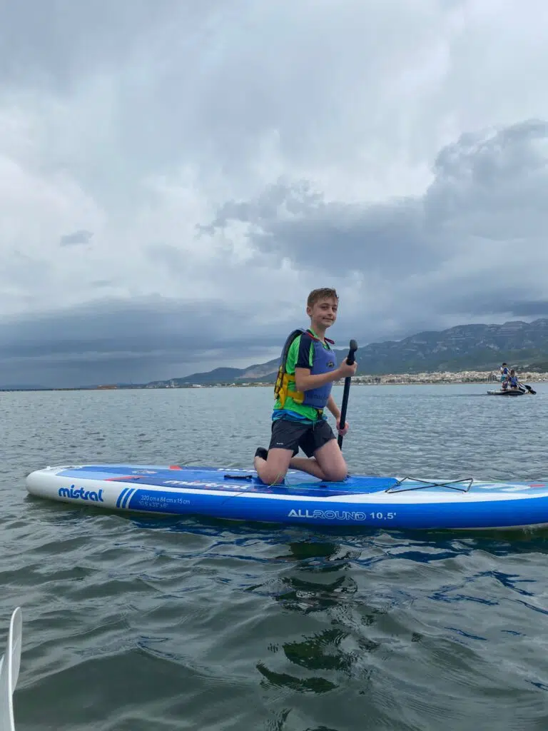 niño de rodillas en una tabla de paddle surf en el mar un día nublado
