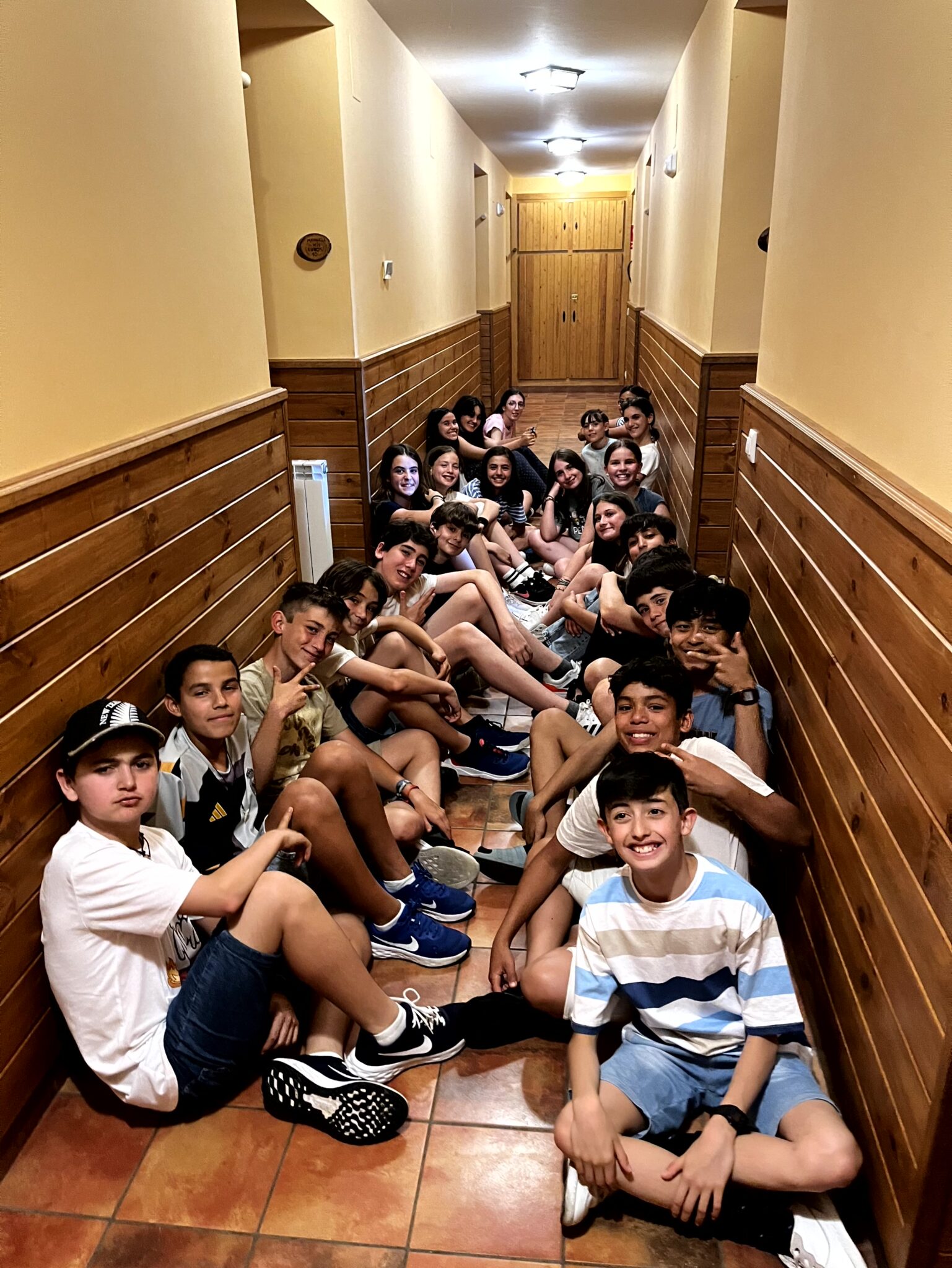 grupo de chavales sentados y sonrientes en un pasillo de un albergue