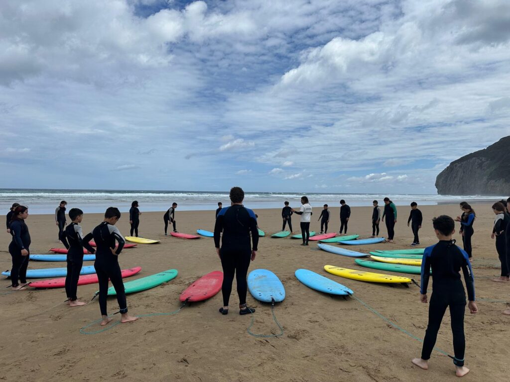 tablas de surf dispuestas en circulo y detrás de ellas chicos y chicas con neoprenos en la playa