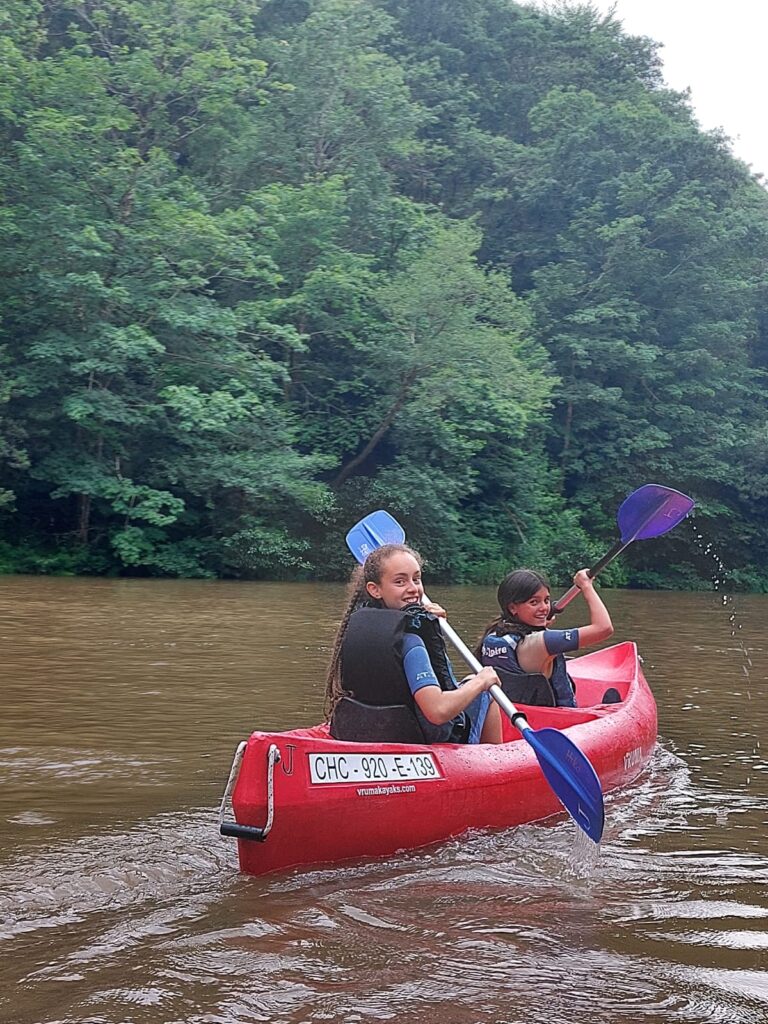 alumnas de primaria en una piragua roja en un rio, con árboles al fondo