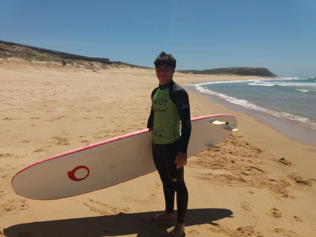 chaval con neopreno en una playa con tabla de surf blanca