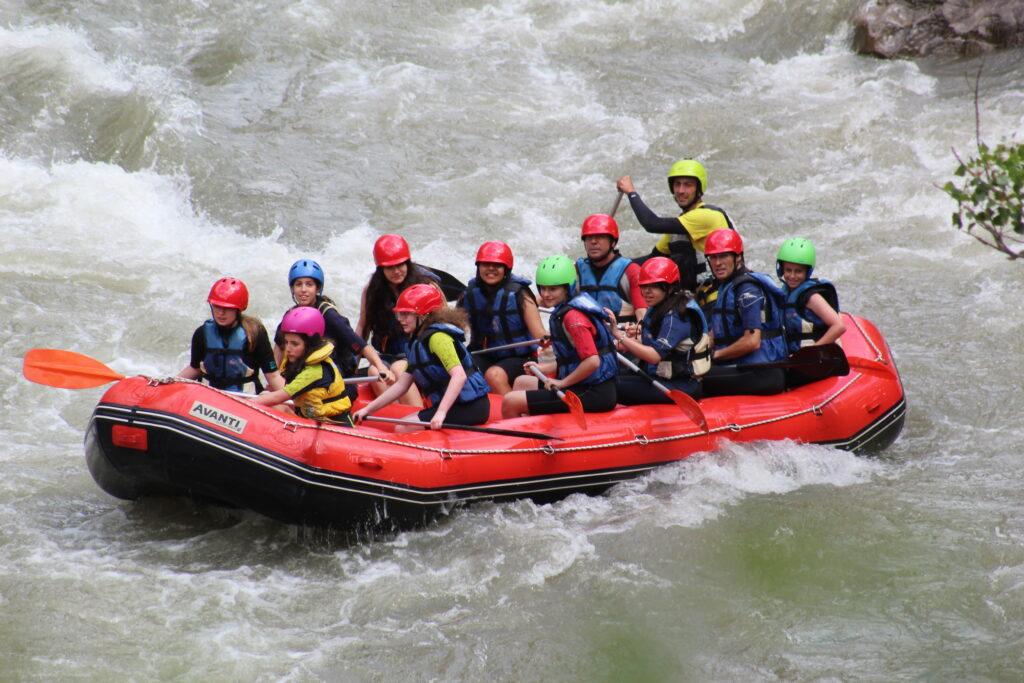 barca con chicos y chicas de secundaria haciendo rafting con monitor, todos con cascos de diferentes colores