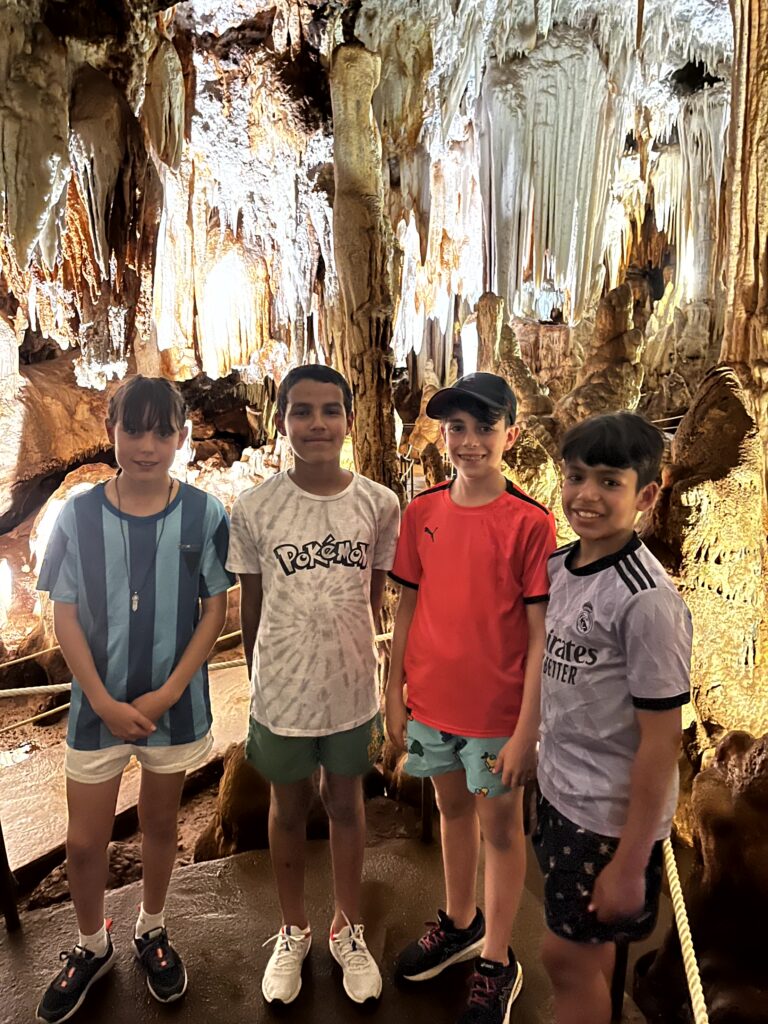 tres chicos, uno de ellos con gorra, y una chica dentro de una cueva con estalactitas